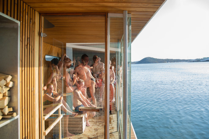 People enjoying a glass-fronted sauna beside the fjord at Sukkerbiten.