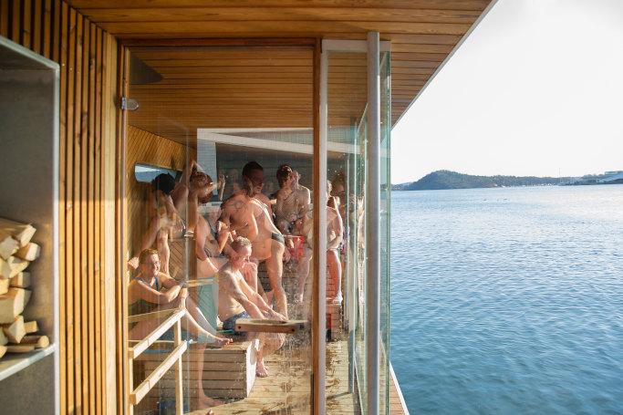 People enjoying a glass-fronted sauna beside the fjord at Sukkerbiten.